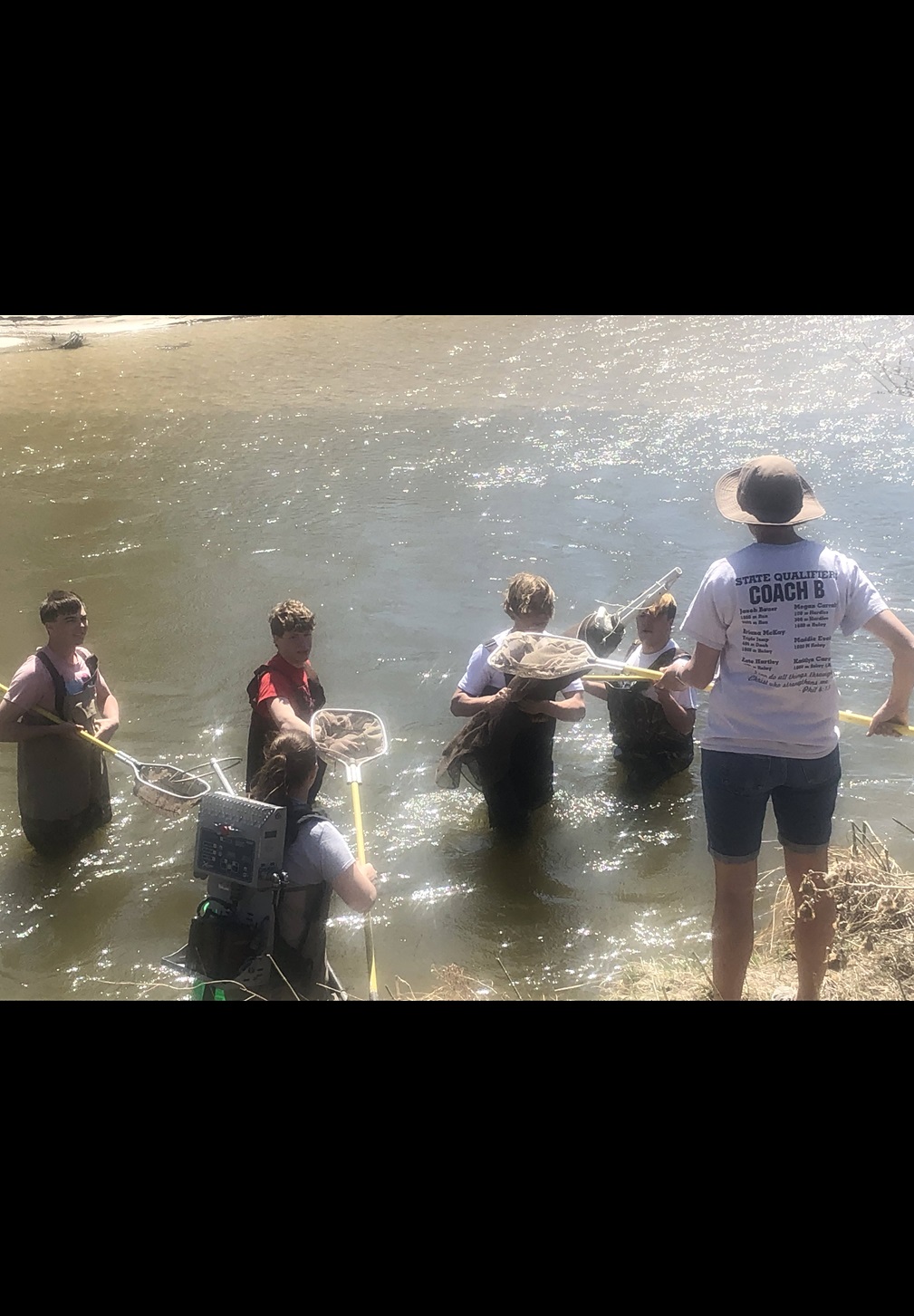 Spalding Academy students (in water) get instruction from their science teacher, Stacey Bauer (on land), as they study local water quality and learn citizen science.