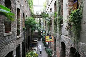 View of the Passageway, and interior shopping area in a historic brick building with plants dangling from all the surrounding openings.