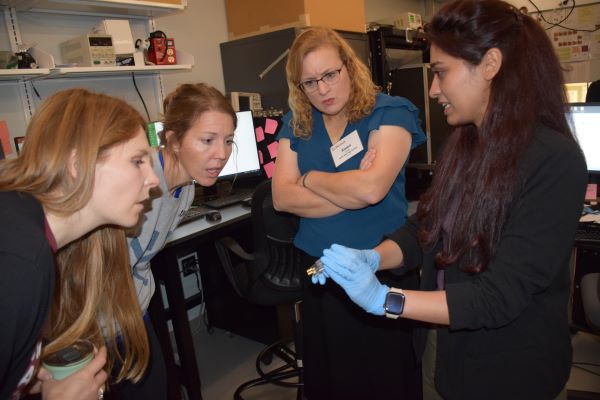 three teachers look closely at a device held by a scientists with gloved hands